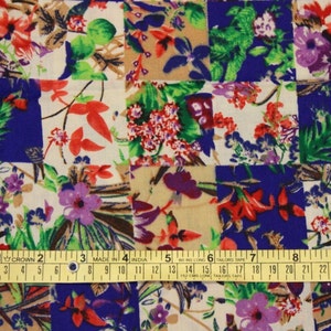 May include: A patchwork fabric with a floral pattern in shades of red, green, purple, and white on a blue and beige background. The fabric is measured with a yellow tape measure.