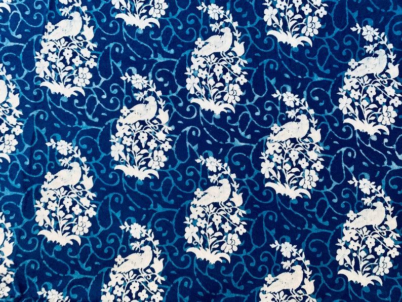 May include: A blue fabric with a white repeating pattern of birds perched on branches with flowers. The pattern is a traditional design.