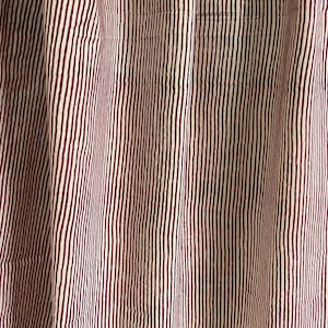 May include: Close-up of a fabric with vertical stripes. The stripes alternate between a cream color and a deep burgundy. The fabric is slightly wrinkled, suggesting it is a curtain or drapery.
