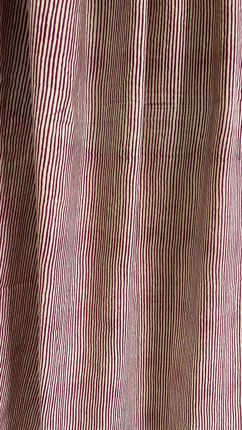 May include: Close-up of a fabric with vertical stripes. The stripes alternate between a cream color and a deep burgundy. The fabric is slightly wrinkled, suggesting it is a curtain or drapery.