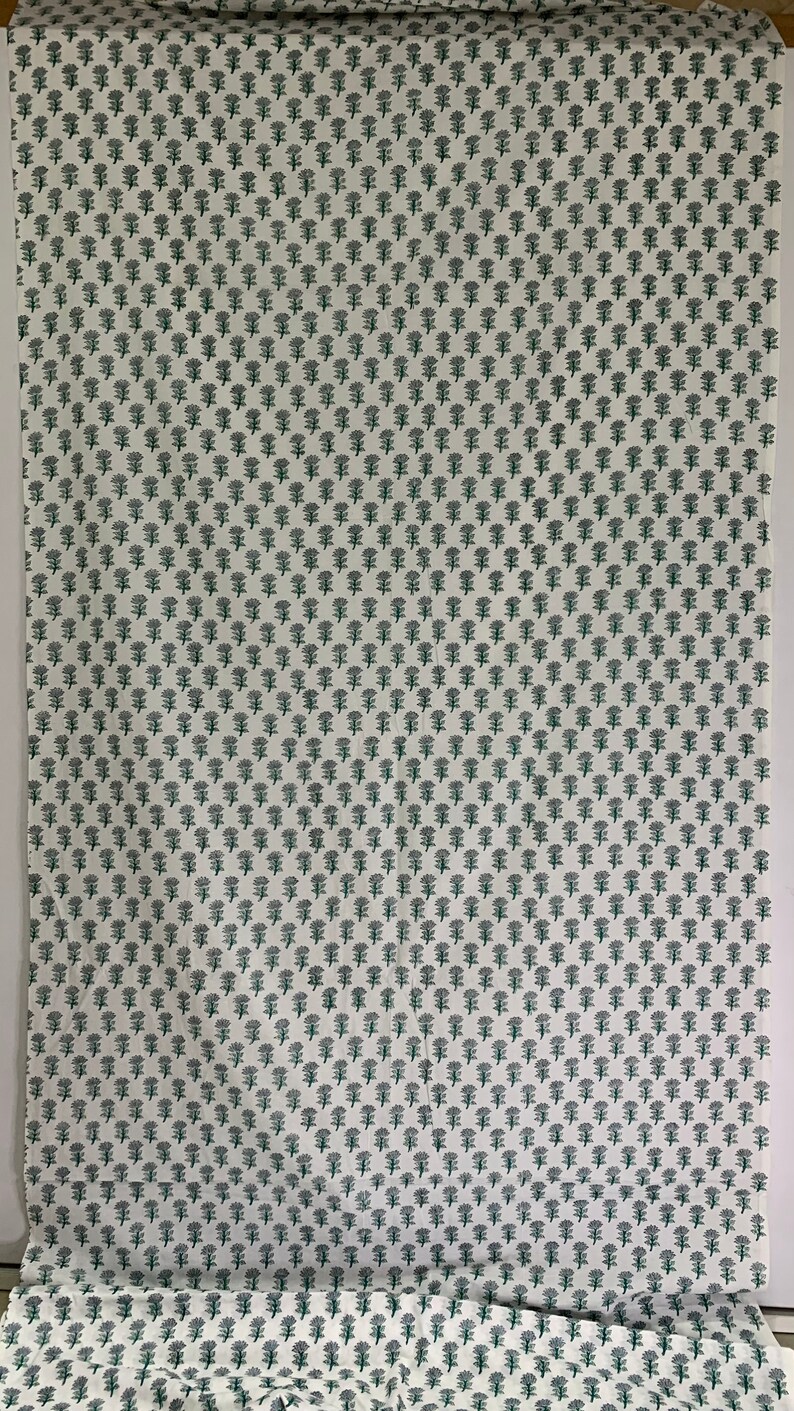 May include: White fabric with a repeating pattern of small green stylised trees. The fabric is folded in half.