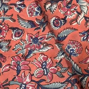 May include: A pink fabric with a floral pattern. The flowers are in shades of pink, blue, and white. The fabric has a vintage feel.