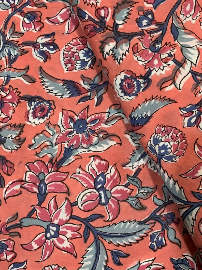 May include: A pink fabric with a floral pattern. The flowers are in shades of pink, blue, and white. The fabric has a vintage feel.