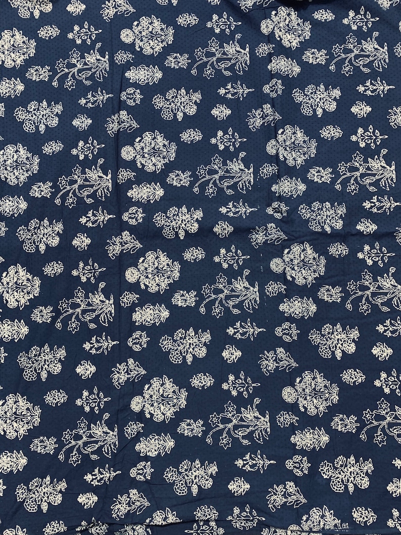 May include: A navy blue fabric with a white floral pattern. The fabric is covered in a repeating pattern of small white flowers and leaves.