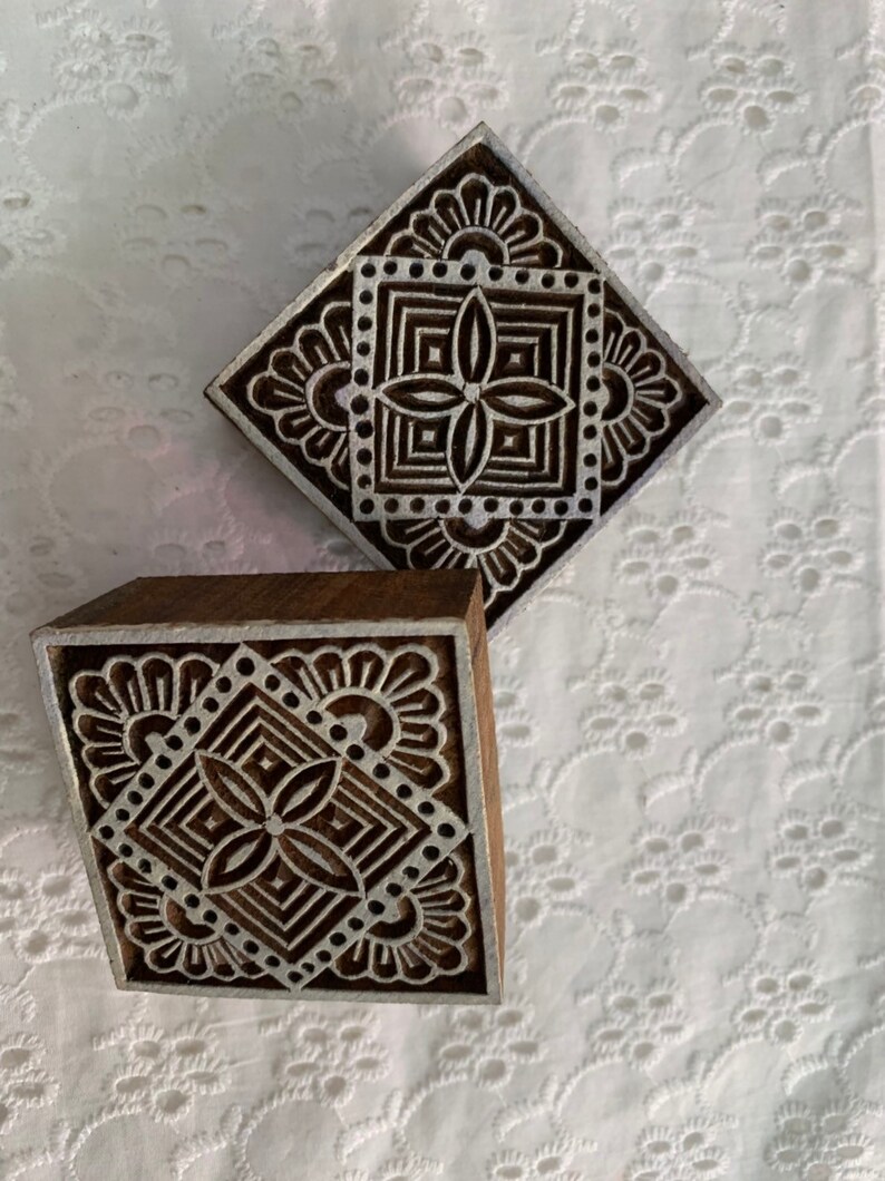 May include: Two wooden printing blocks with intricate, symmetrical designs. The blocks feature a square pattern with floral and geometric elements, perfect for textile or paper crafts. The wood has a natural brown color, and the design is in white.