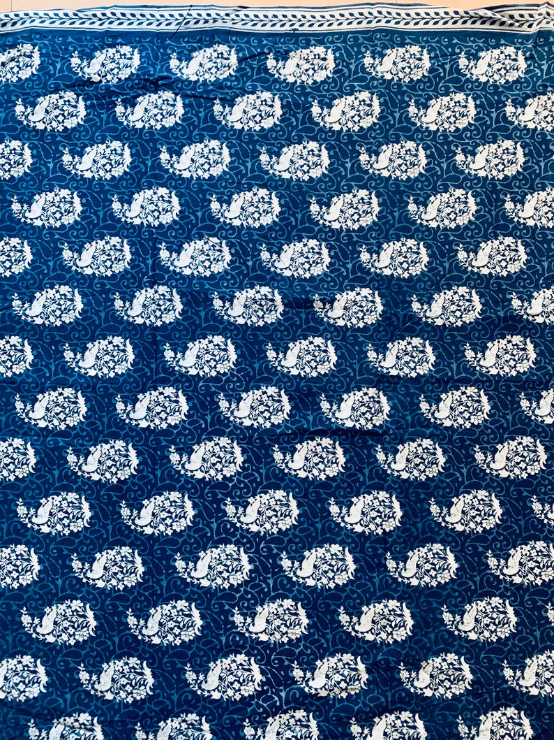 May include: A blue fabric with a white paisley pattern. The fabric has a white border with a repeating leaf design.