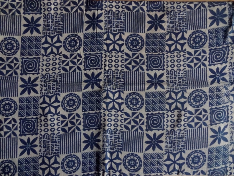 May include: A white fabric with a repeating pattern of blue geometric shapes and flowers. The pattern includes circles, squares, triangles, and stars.