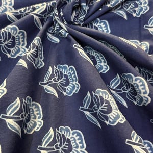 May include: A close-up of a blue fabric with a white floral pattern. The fabric is soft and has a subtle texture.