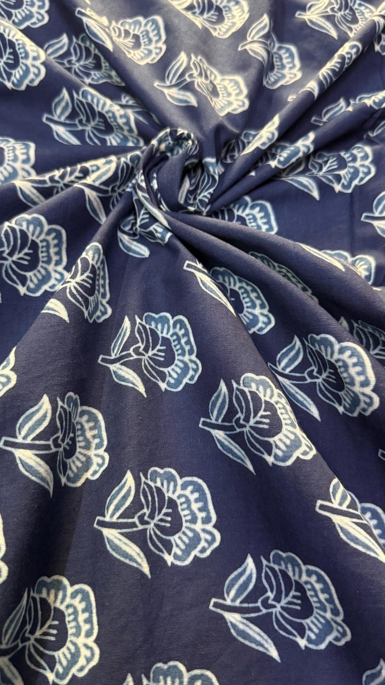 May include: A close-up of a blue fabric with a white floral pattern. The fabric is soft and has a subtle texture.