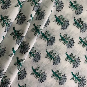 May include: White cotton fabric with a repeating pattern of green and grey floral sprigs. The fabric is folded in a diagonal pattern.