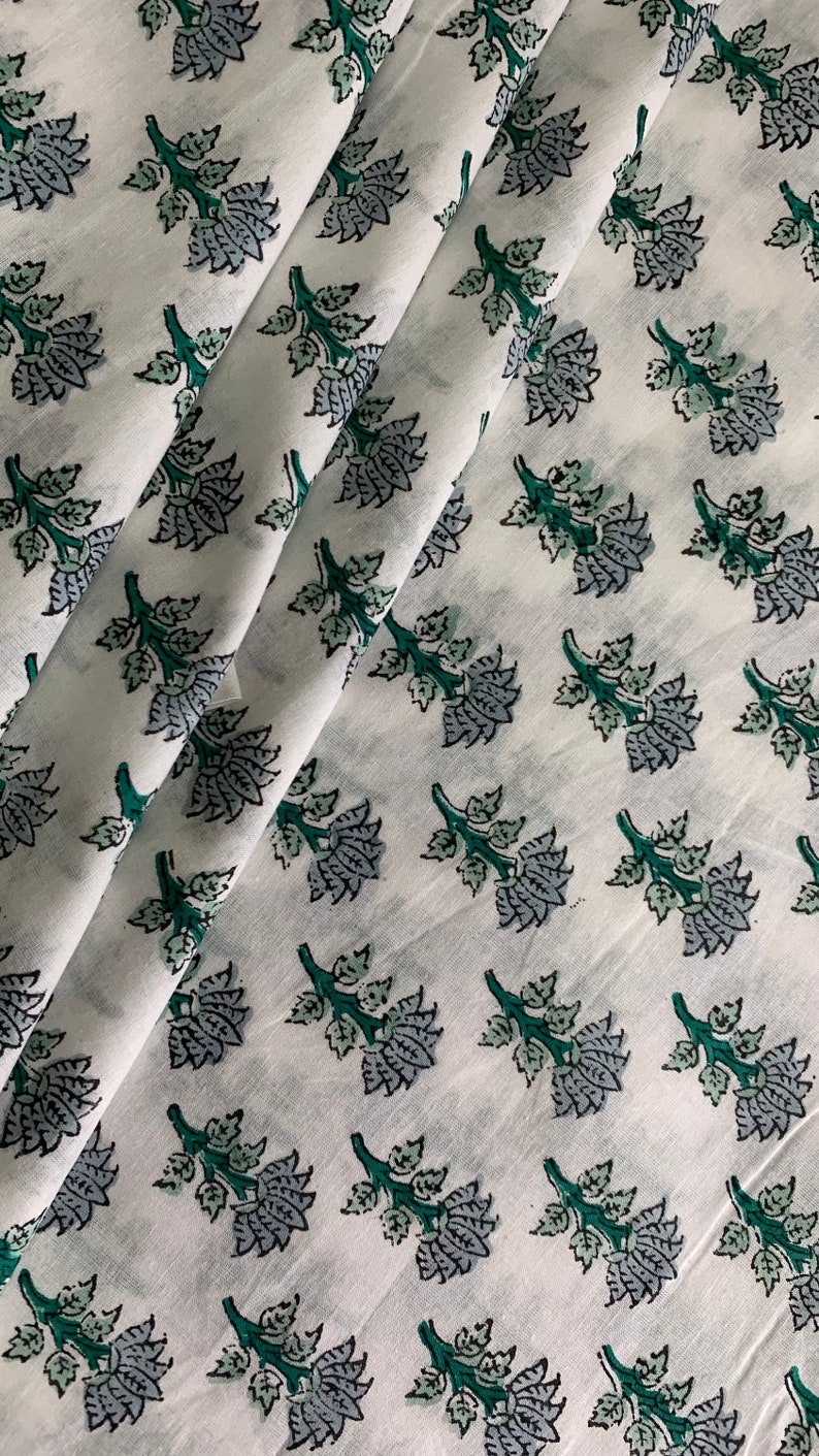May include: White cotton fabric with a repeating pattern of green and grey floral sprigs. The fabric is folded in a diagonal pattern.