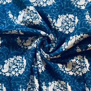 May include: A blue fabric with a white floral pattern. The fabric is folded and has a textured surface.