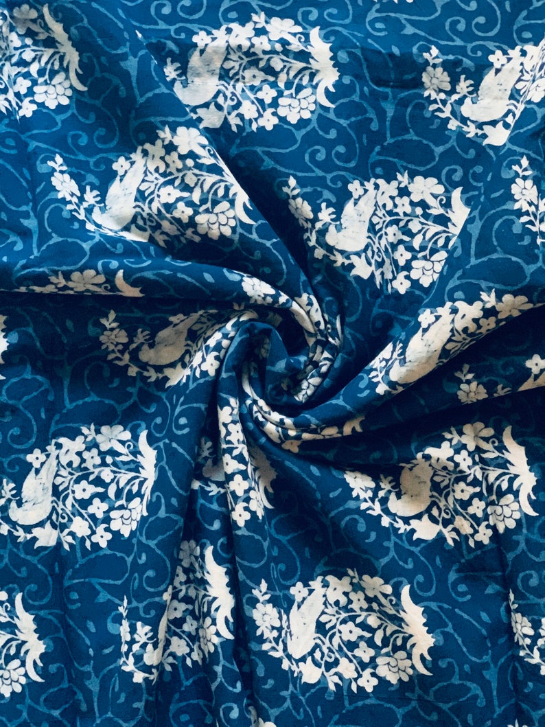May include: A blue fabric with a white floral pattern. The fabric is folded and has a textured surface.