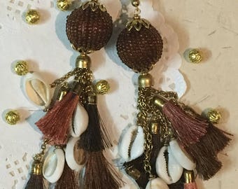 May include: Two brown beaded tassel ornaments with gold accents and white seashells. Each tassel features brown, black, and pink strands.