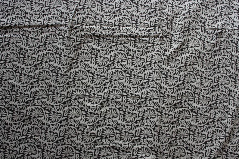 May include: Black and white fabric with a repeating floral pattern. The fabric has a subtle sheen and a soft texture.