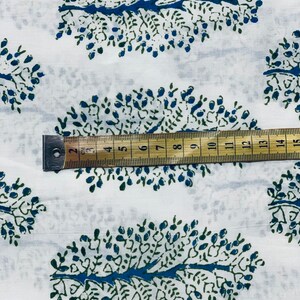 May include: White fabric with a repeating pattern of blue and green stylized trees. A ruler is placed on the fabric, showing measurements in inches.