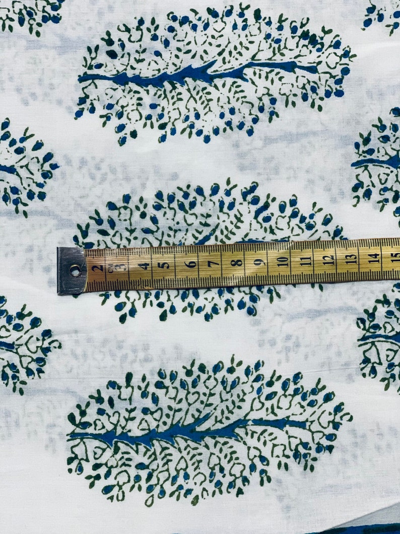 May include: White fabric with a repeating pattern of blue and green stylized trees. A ruler is placed on the fabric, showing measurements in inches.
