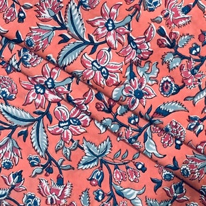 May include: A pink fabric with a floral pattern. The flowers are in shades of pink, blue, and white. The fabric has a vintage feel.
