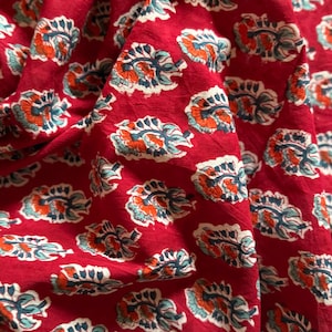 Op de afbeelding: Rode stof met een herhalend patroon van blauwe, witte en oranje bloemenmotieven.