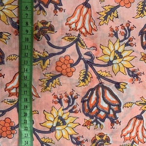 May include: Pink fabric with a floral print featuring orange, yellow, and white flowers with gray stems and leaves. The fabric is measured with a ruler in inches.