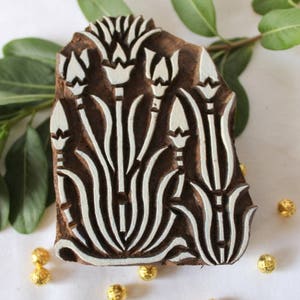 May include: A wooden printing block with a floral design. The block is carved with a pattern of stylized flowers and leaves. The design is in white against a dark brown background.