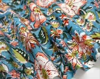 May include: A piece of fabric featuring a light blue background with a repeating floral pattern in shades of coral, white, and green. The textile displays a dense arrangement of stylized blossoms and leaves, with soft folds creating depth across the surface.