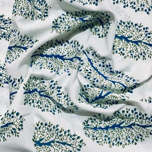 May include: White fabric with a blue and green tree pattern. The fabric is folded and has a textured surface.