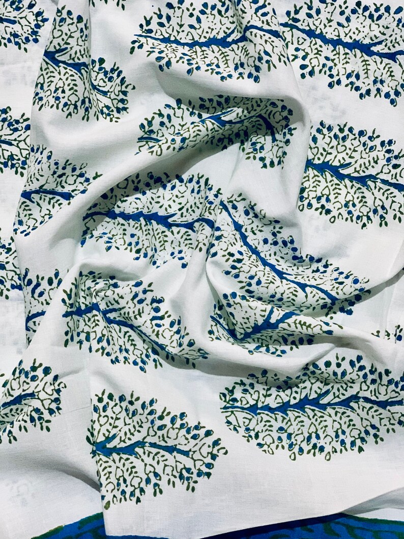 May include: White fabric with a blue and green tree pattern. The fabric is folded and has a textured surface.