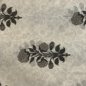 May include: White fabric with a repeating pattern of black floral designs. The floral pattern features stylized leaves and flowers.