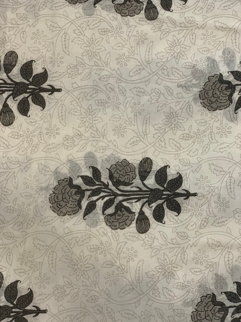 May include: White fabric with a repeating pattern of black floral designs. The floral pattern features stylized leaves and flowers.
