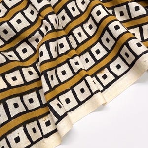 Puede incluir: Una tela textil con un patrón geométrico repetitivo de rayas horizontales color amarillo mostaza que alternan con filas de cuadrados blancos delineados en negro, cada uno con un pequeño cuadrado negro sólido en el centro del cuadrado blanco.