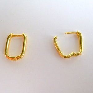 May include: A pair of gold hoop earrings. The earrings are rectangular in shape and have a slightly curved design.