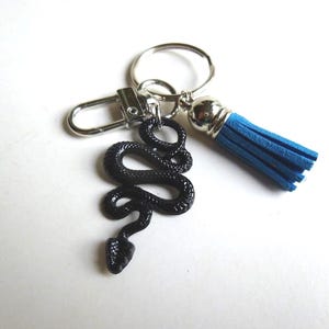 May include: A black snake charm keychain with a silver clasp, ring, and tassel. The tassel is blue. The snake charm is detailed and textured.