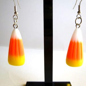 May include: Candy corn earrings with silver-tone hooks. Each earring features a candy corn design with white, orange, and yellow layers. These Halloween-themed earrings are a fun accessory.