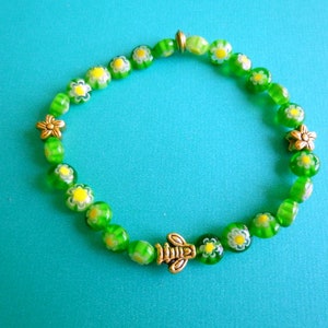 May include: A green and yellow beaded bracelet with a bee charm. The beads are decorated with small white flowers.