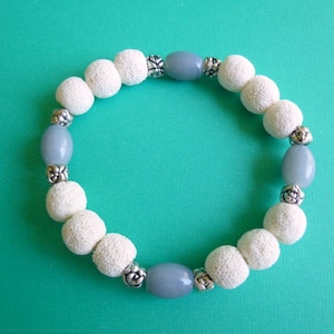 Op de afbeelding: Een witte en grijze kralen armband met zilveren accenten. De armband is gemaakt met lavastenen kralen en grijze glazen kralen.