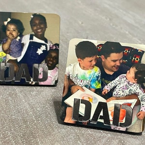 May include: Two photo coasters with the word "DAD" in large, bold letters. The first coaster features a photo of a woman with three children. The second coaster features a photo of a man with two children.