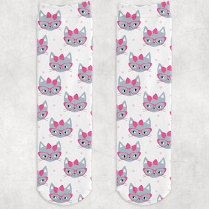 May include: A pair of white socks with a repeating pattern of gray cats wearing pink bows and glasses. The cats are on a white background with small pink dots.