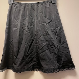 May include: Black slip skirt hanging on a black hanger. The skirt is made of a shiny fabric and has a lace trim at the hem. The hanger is marked "XL".