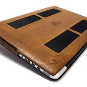 May include: A brown leather laptop case with black mesh panels for ventilation. The case has a silver zipper and a silver trim around the edges.