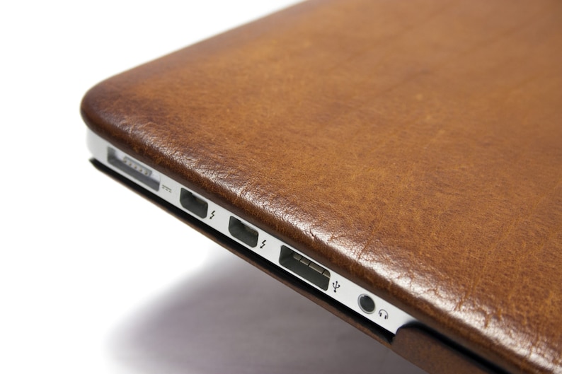 May include: A brown leather laptop case with a silver trim and ports on the side.