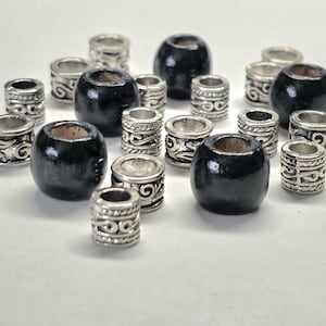 May include: A collection of jewelry beads consisting of smooth, round black beads and cylindrical silver-toned metal beads featuring intricate embossed scrollwork patterns. The beads are scattered in a group, displaying a mix of dark and metallic finishes.