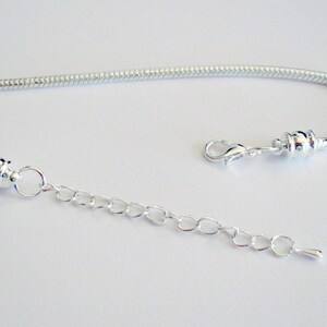 May include: A silver chain bracelet with a lobster clasp and an extender chain. The bracelet is made of a snake chain style.