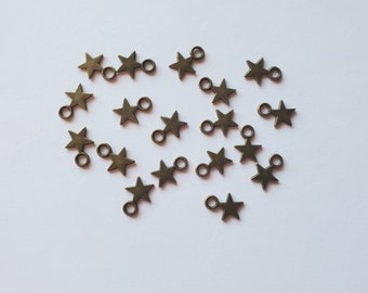 May include: A collection of small, bronze-colored star charms with attached jump rings. The charms are scattered on a white surface, each star having five points and a loop for attaching to jewelry or other crafts.