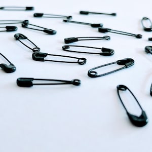 100 imperdibles negros muy pequeños de 19 mm de largo. Imperdibles de aleación metálica.