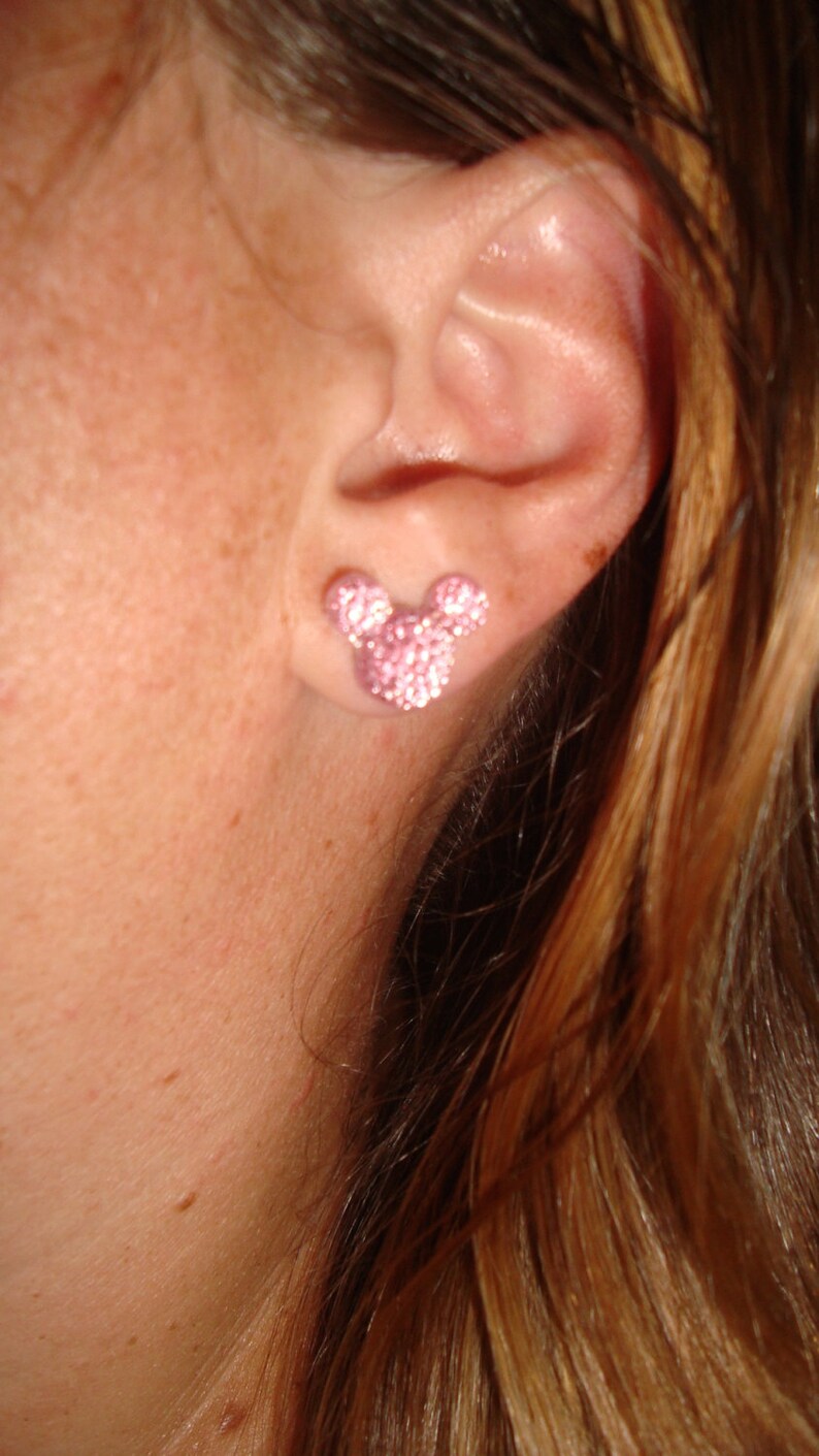 Op de afbeelding: Een close-up van iemands oor met een roze, glinsterende Mickey Mouse oorbel.