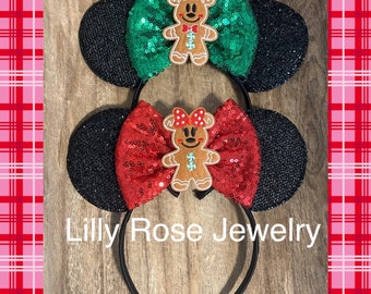 Puede incluir: Dos diademas negras con orejas de ratón con lentejuelas, un hombre de jengibre y un lazo con lentejuelas. Un lazo es verde, el otro es rojo. El texto "Lilly Rose Jewelry" está impreso en la diadema.