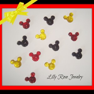 May include: A collection of 12 Mickey Mouse head-shaped rhinestones in red, yellow, and black. The rhinestones are arranged in a grid pattern on a white background. The text "Lilly Rose Jewelry" is visible in the bottom right corner of the image.