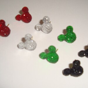 Op de afbeelding: Een set van tien Mickey Mouse-vormige oorbellen in verschillende kleuren, waaronder rood, groen, zwart en wit. Elke oorbel is gemaakt van strass en heeft een kleine pen om aan een oor te bevestigen.