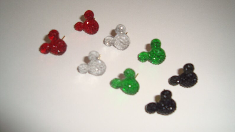 Op de afbeelding: Een set van tien Mickey Mouse-vormige oorbellen in verschillende kleuren, waaronder rood, groen, zwart en wit. Elke oorbel is gemaakt van strass en heeft een kleine pen om aan een oor te bevestigen.
